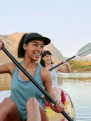 Two smiling friends kayaking on a lake together during summer break. Smiling and happy playful women bonding outside in nature with water activity. Having fun on a kayak during weekend recreation.